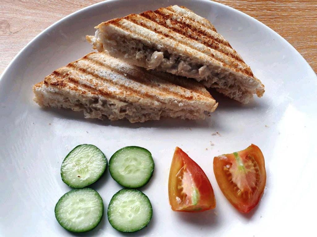 A Filipino style chicken sandwich spread that is sliced into two served with slices of cucumber and tomatoes
