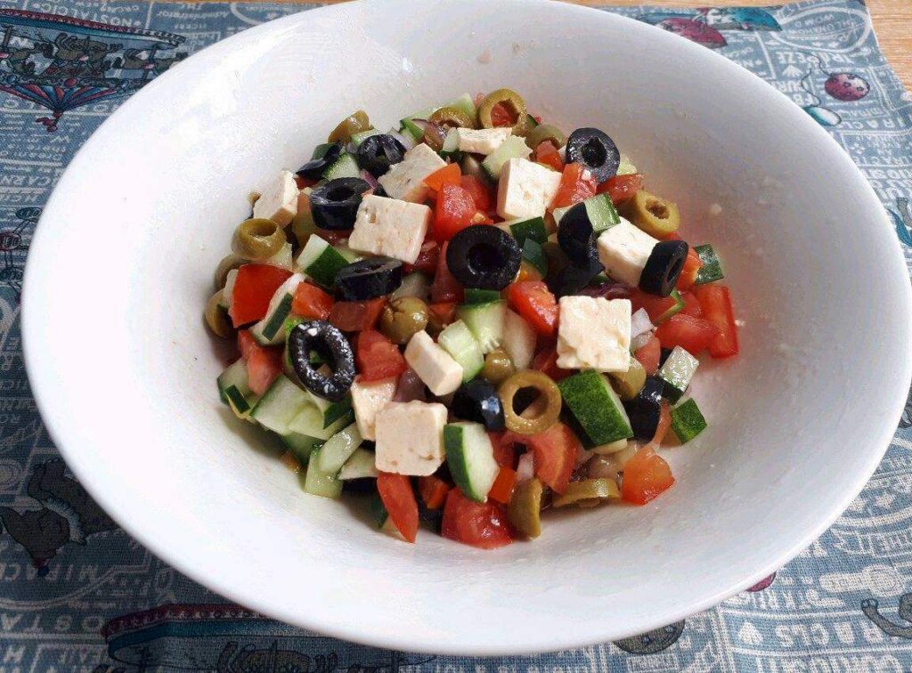 A Shepherd Salad Recipe mix with feta cheese, olives, tomatoes, and cucumber in a large bowl