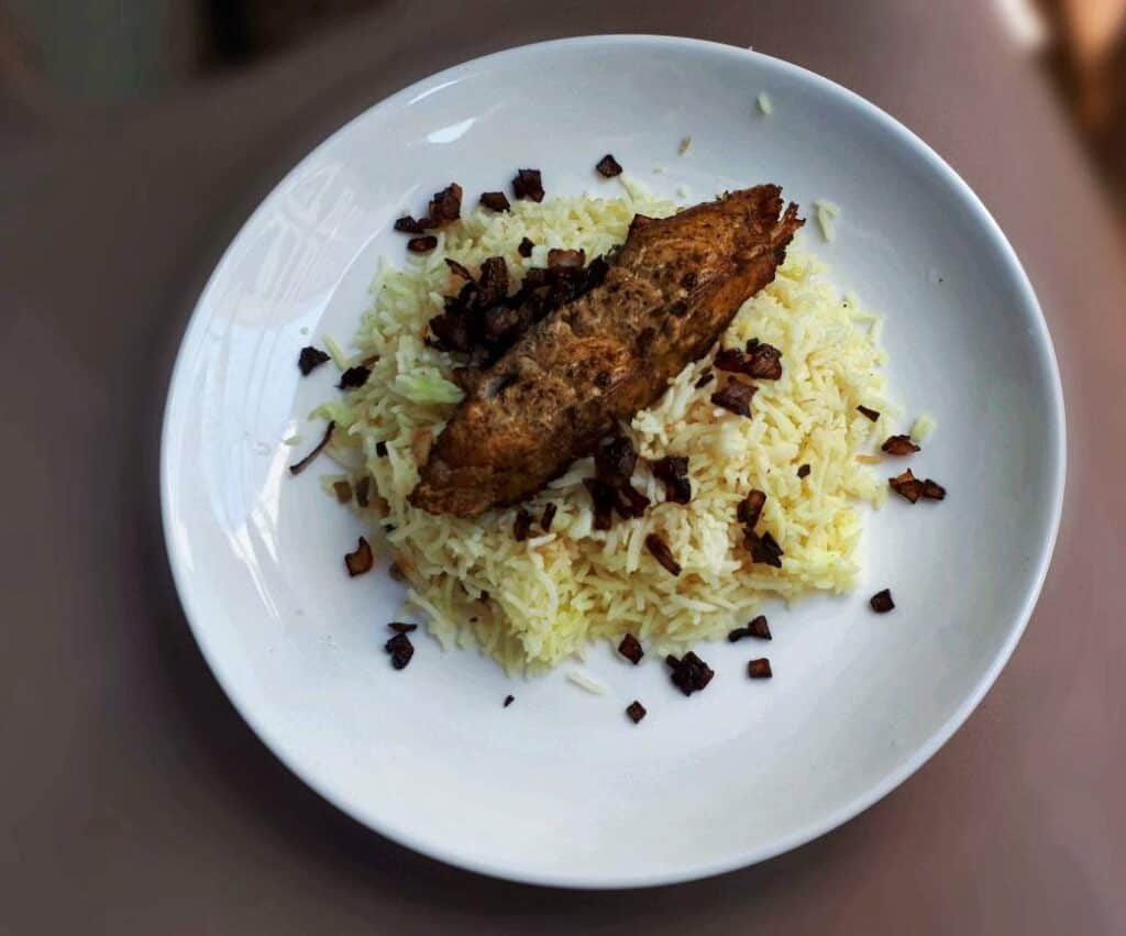 Fish Machboos mixed with turmeric basmati rice, boneless spanish mackerel fish. and garnished with fried brown onion 