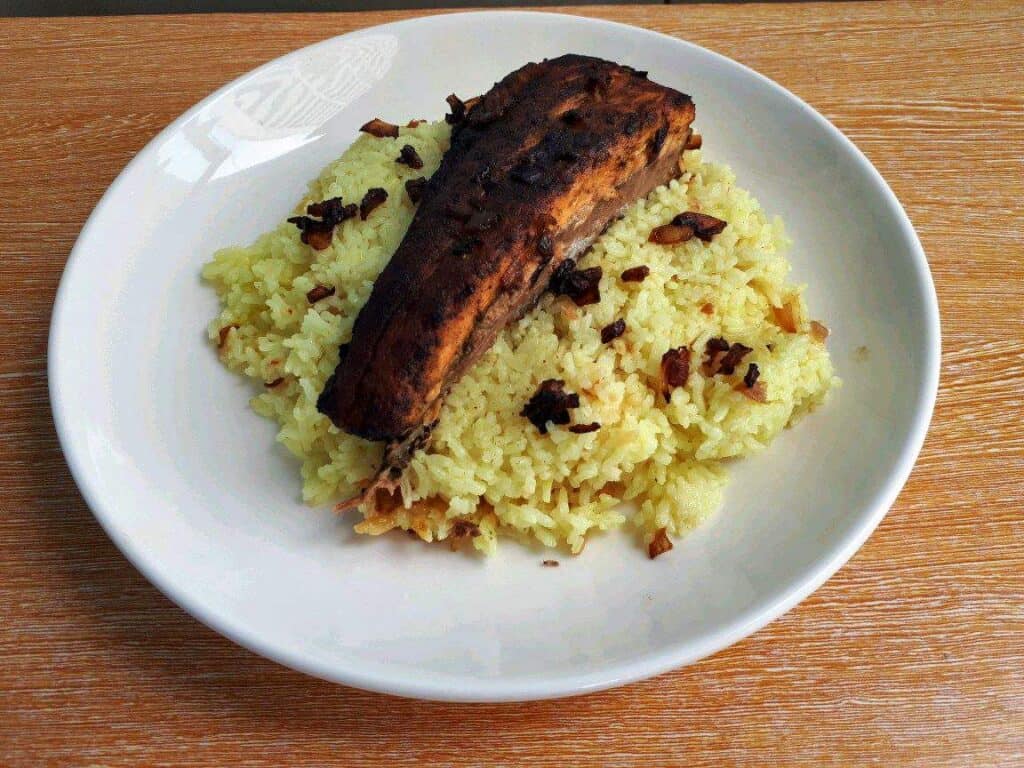 Fish Machboos mixed with turmeric basmati rice, salmon fillet, and garnished with fried brown onion