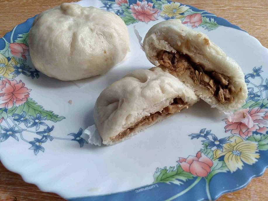 A white steamed bun filled with chicken siopao asado filling serve on a plate.