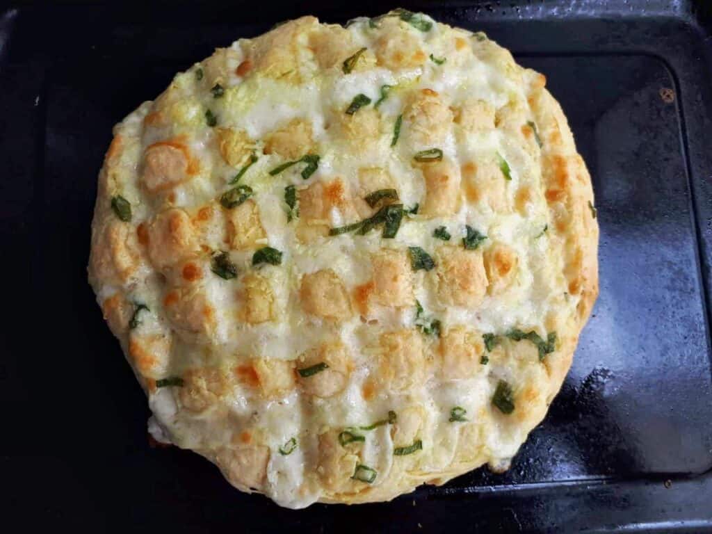 Garlic Mozzarella bread mixed with cheese and spread with garlic green onion butter in a tray.