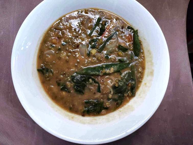 A filipino mung bean soup Ginisang Monggo mixed with spinach and green beans served in a plate bowl.