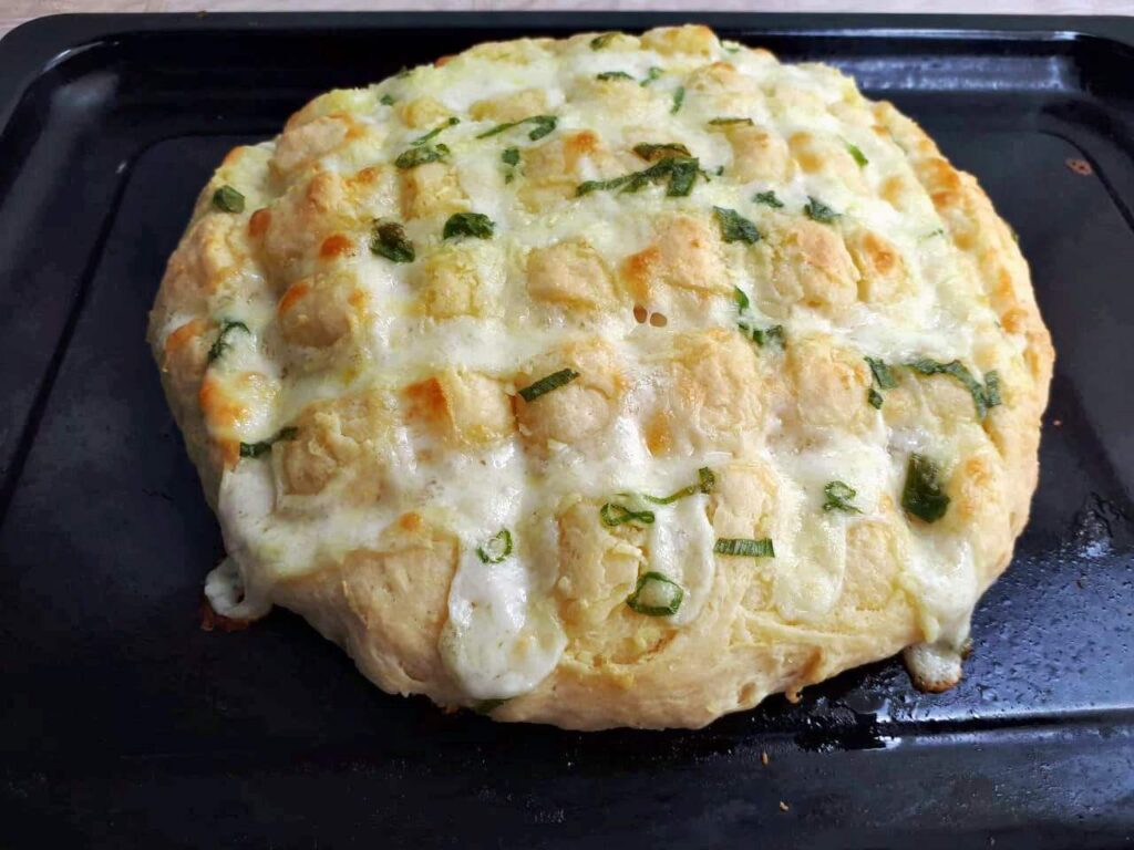 Garlic Mozzarella bread mixed with cheese and spread with garlic green onion butter in a tray.