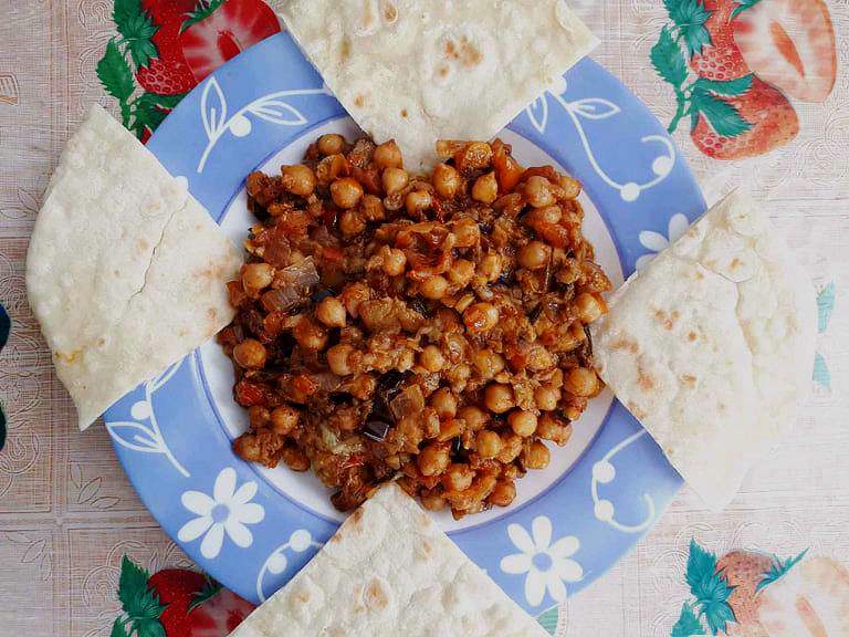Lebanese Moussaka or Maghmour vegan eggplant recipe mixed with chickpeas, onion, garlic, and tomatoes with 4 slices of pita bread serve on a plate.
