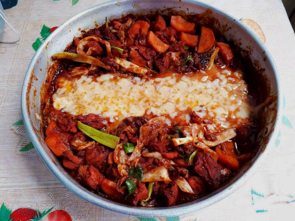 A spicy korean chicken dish called Cheese Dakgalbi mixed with boneless chicken, carrots, spring onion and mozzarella cheese in a round pan