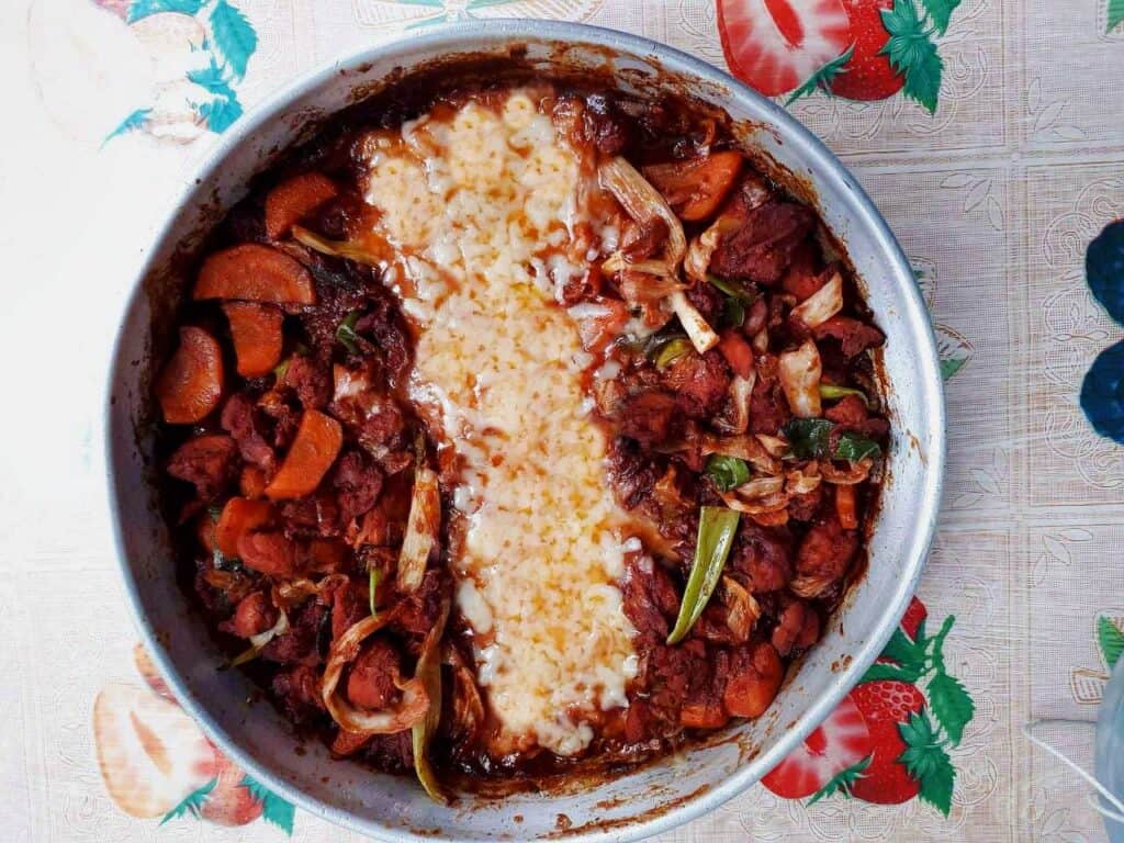 A spicy Korean chicken dish called Cheese Dakgalbi mixed with boneless chicken, carrots, spring onion and mozzarella cheese in a round pan