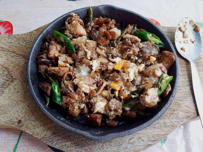 A filipino chicken sisig that is mixed with chicken liver & breast and green chilies serve in a caster iron plate.