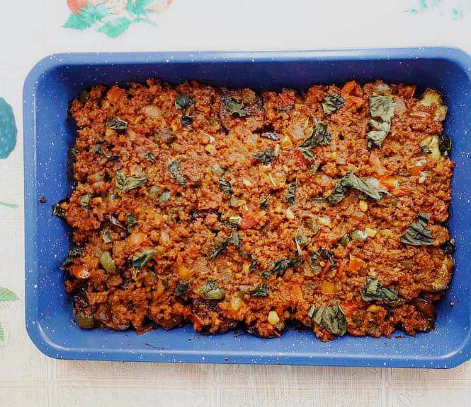 A Turkish moussaka dish mixed with ground beef, tomato sauce, eggplant and chopped basil leaves on a baking tray
