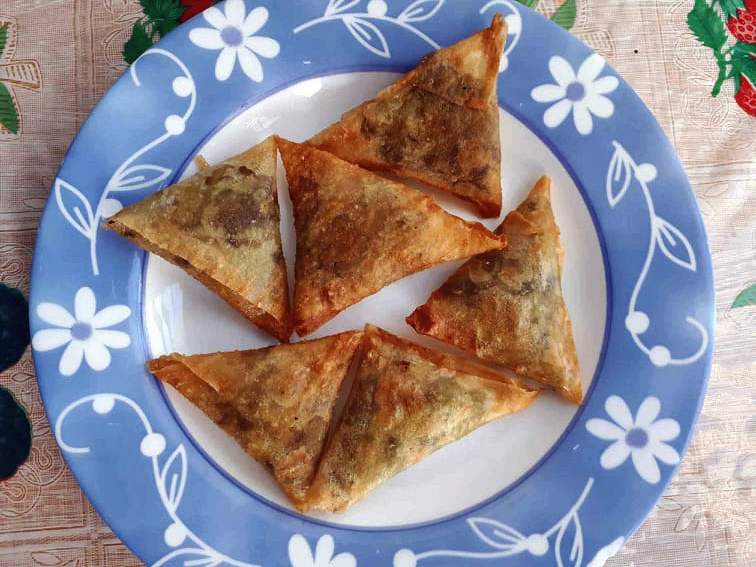 A triangular-shaped deep fried Indian pastry dish called Vegetable samosas serve on a plate