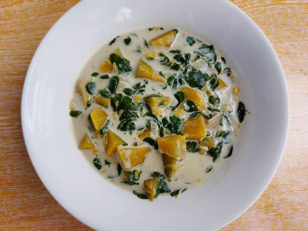 A Filipino vegetarian stew recipe Ginataang Kalabasa mixed with coconut milk, squash, and malunggay (moringa) leaves served on a plate bowl.