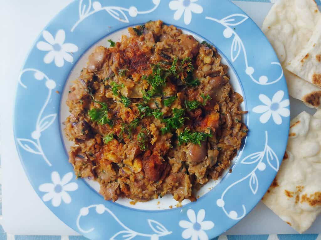 Egyptian Fava Bean Recipe Ful Medames that is topped with chopped parsley leaves and served with pita bread.