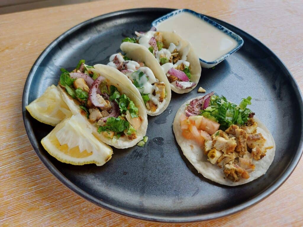 Shawarma Tacos with filling of chopped chicken shawarma, parsley, red onion & tomatoes drizzled with white sauce on a mini tortilla bread