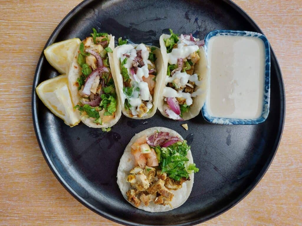 Shawarma Tacos with filling of chopped chicken shawarma, parsley, red onion & tomatoes drizzled with white sauce on a mini tortilla bread