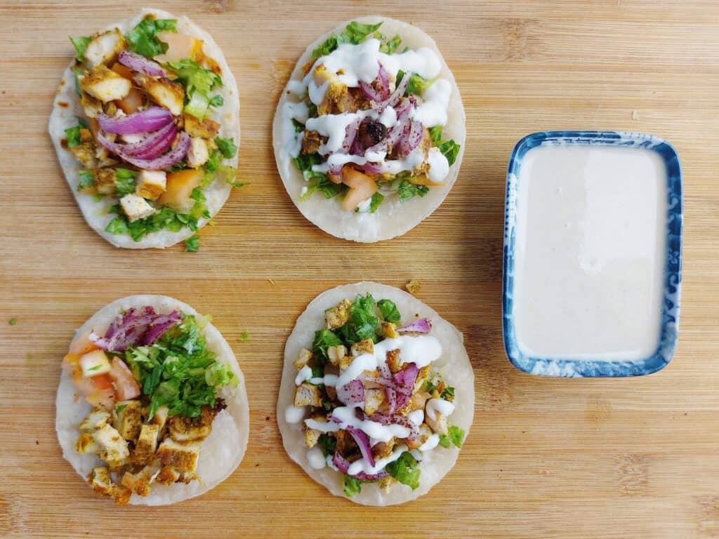 Shawarma Tacos with filling of chopped chicken shawarma, parsley, red onion & tomatoes drizzled with white sauce on a mini tortilla bread