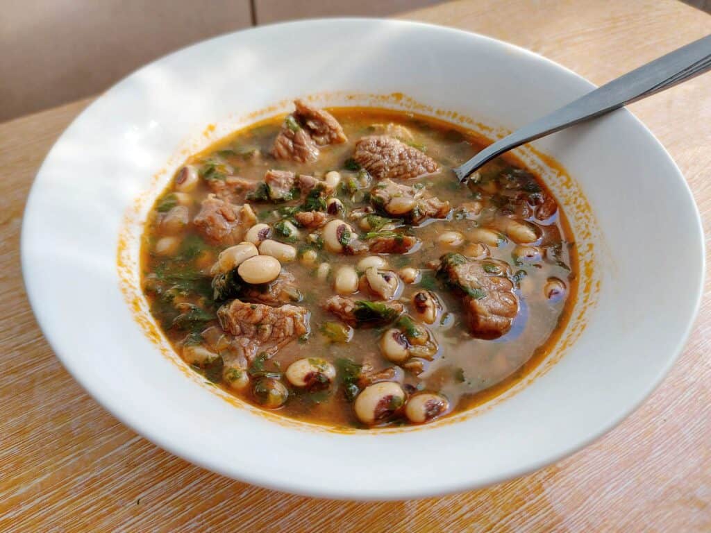 A black eyed bean tomato stew fasolia mixed with beef and chopped coriander leaves served on a plate bowl