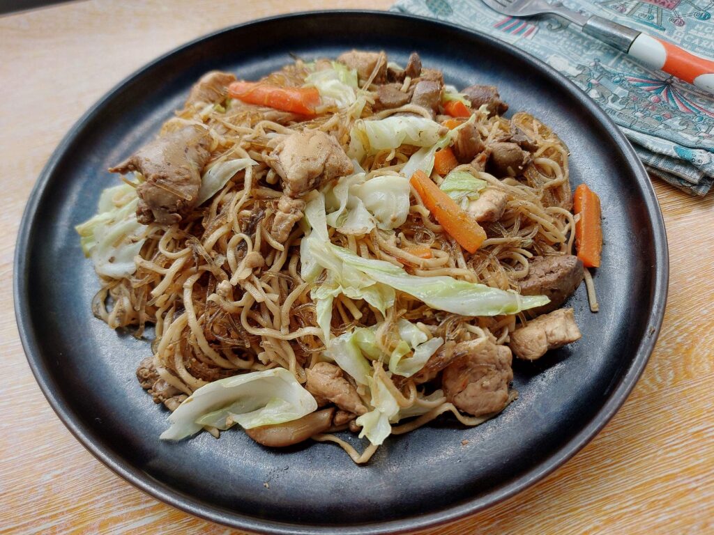 Filipino Pancit Bam-I recipe that is mixed with carrots, chicken breast and liver, cabbages and noodles served on a plate.