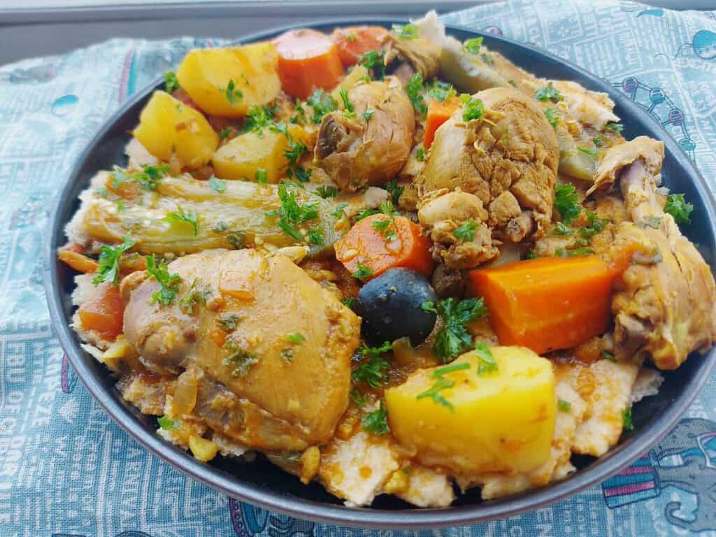 A Kuwaiti Gulf Arabic recipe Tashreeb that is mixed with chicken, potatoes, carrots and eggplant with pieces of flatbread under it and served on a plate.