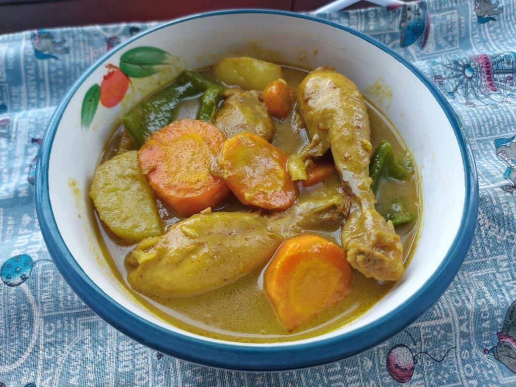 Filipino chicken curry mixed with carrots, potatoes, green bell pepper with chicken leg served in a yellow coconut curry stew in a plate bowl
