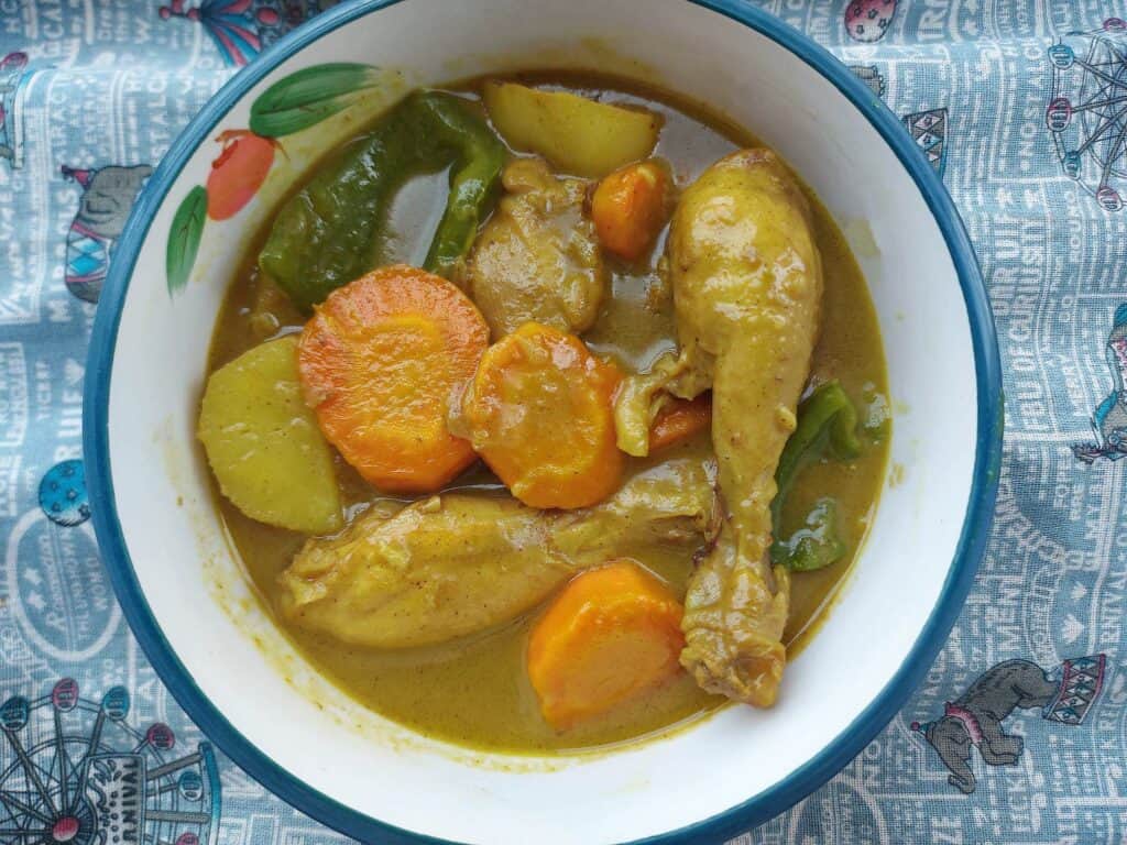 Filipino chicken curry mixed with carrots, potatoes, green bell pepper with chicken leg served in a yellow coconut curry stew in a plate bowl