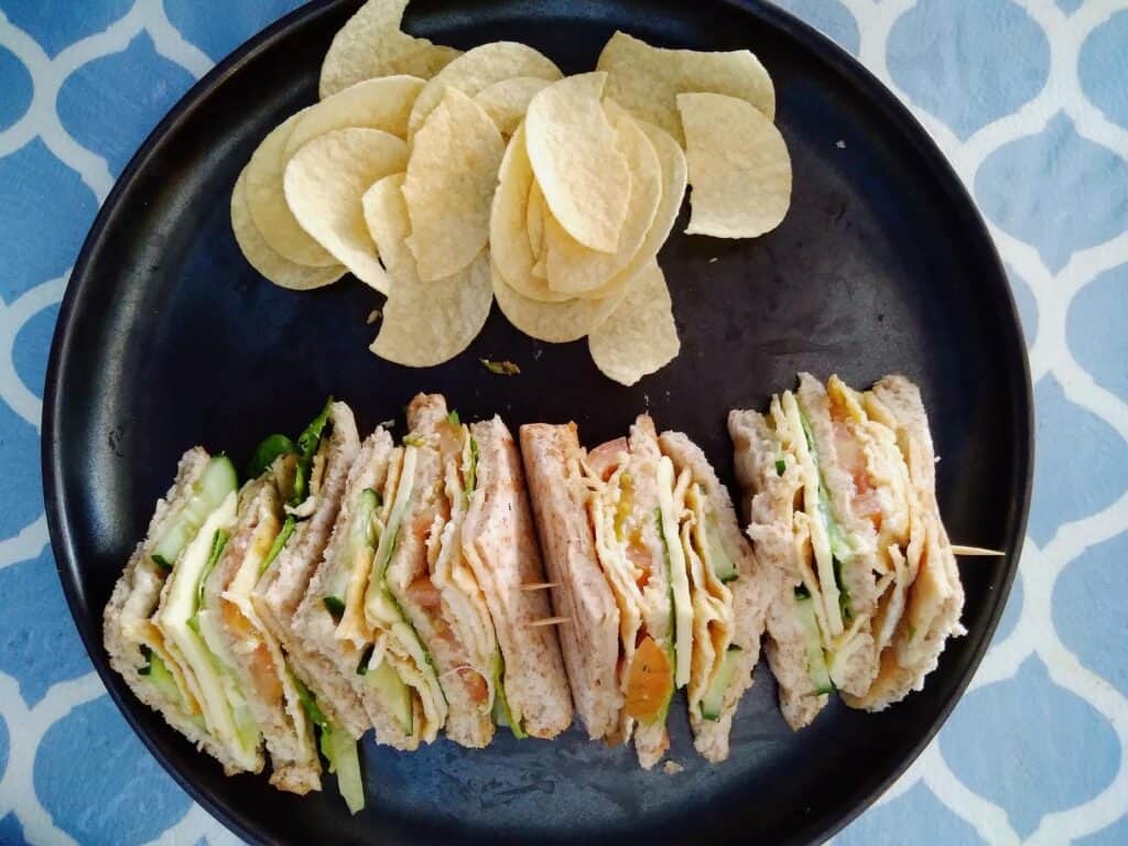 This is a Filipino clubhouse sandwich that contain ham, scrambled egg, lettuce, cucumber, tomatoes, cheese and mayonnaise served with potato chips.