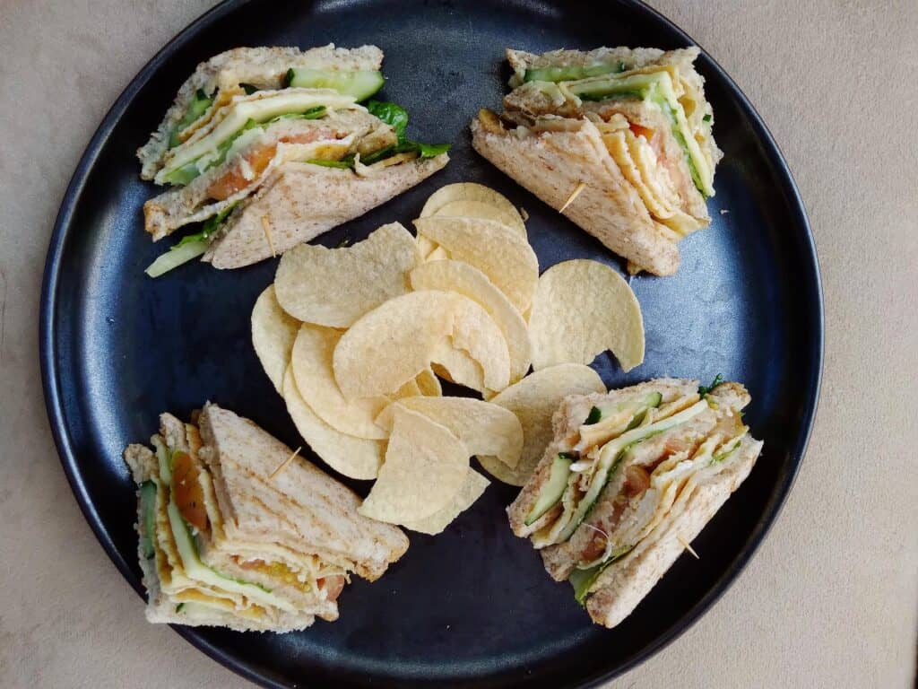 This is a Filipino clubhouse sandwich that contain ham, scrambled egg, lettuce, cucumber, tomatoes, cheese and mayonnaise served with potato chips.