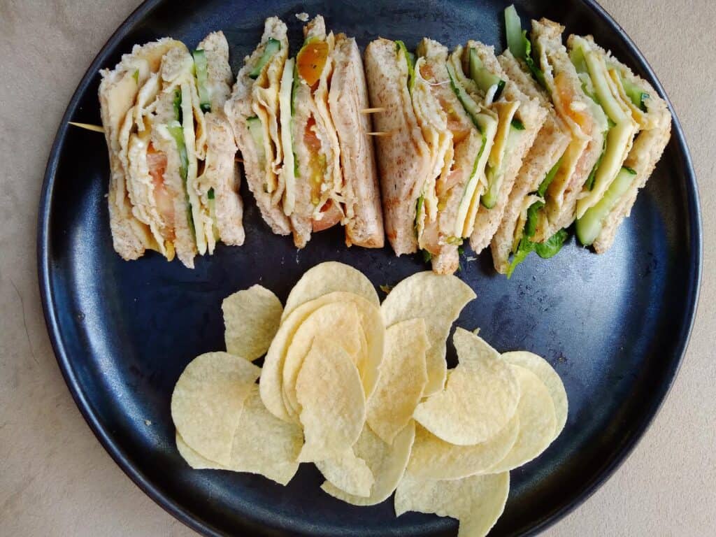 This is a Filipino clubhouse sandwich that contain ham, scrambled egg, lettuce, cucumber, tomatoes, cheese and mayonnaise served with potato chips.