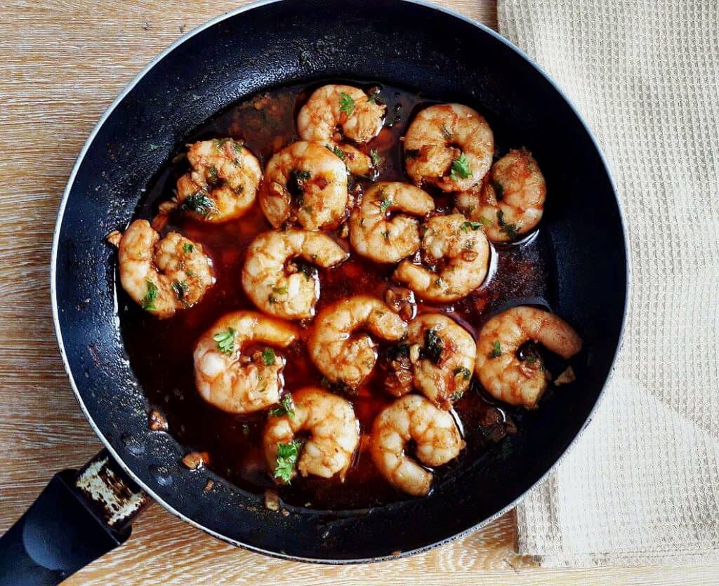 Spanish Garlic Prawns consist of prawns, paprika, garlic, garnished with chopped parsley sautéed in olive oil served in a pan.