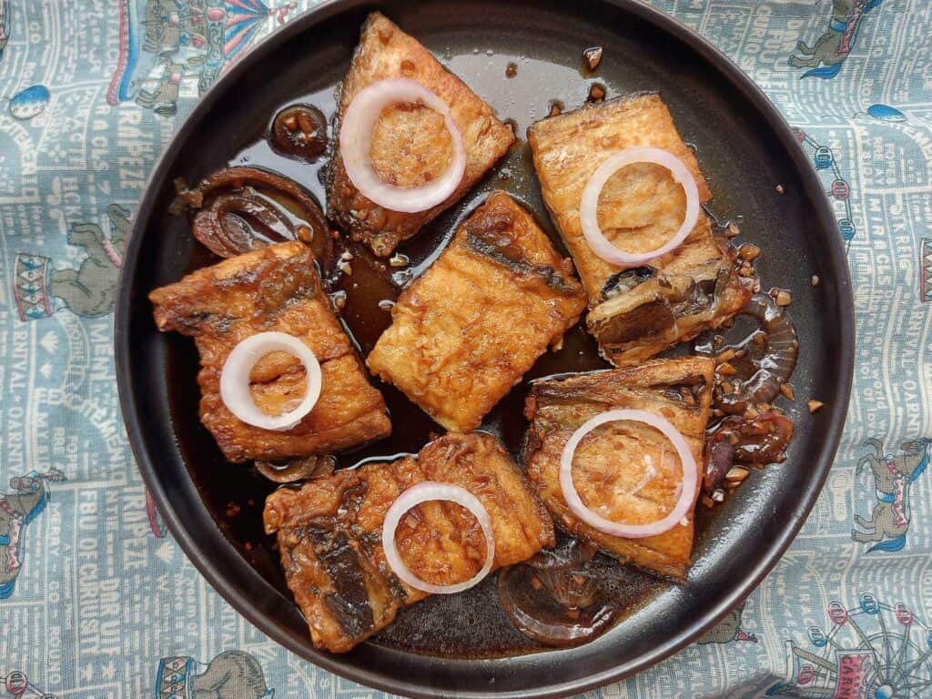 A filipino recipe called Bangus steak cooked in adobo mixture sauce garnished with sliced onion ring served on a plate.
