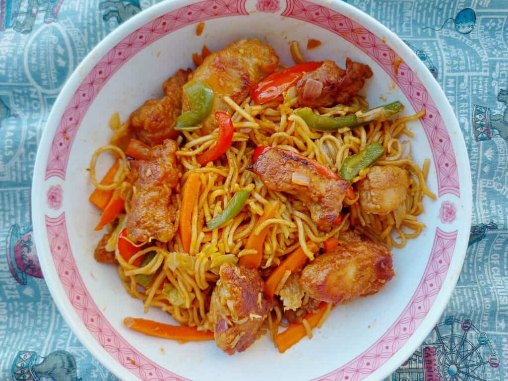 An indo-Chinese Chicken Manchurian noodle recipe mixed with fried boneless chicken breast, noodles, julienned carrots and cabbages served on a plate