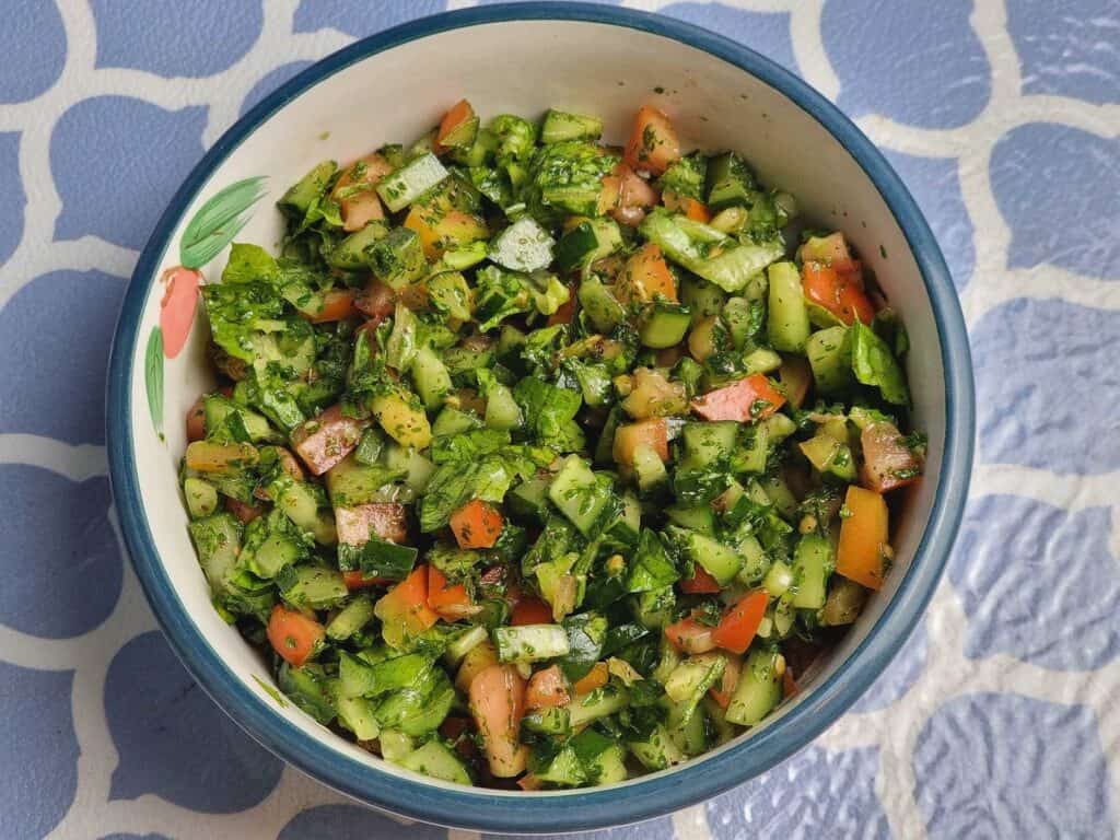 Arabic Salad mixed with cucumber, tomatoes, parsley, olive oil and sumac spices served on a plate bowl.