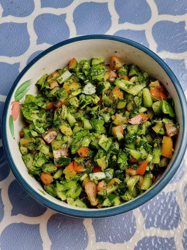Arabic Salad mixed with cucumber, tomatoes, parsley, olive oil and sumac spices served on a plate bowl.