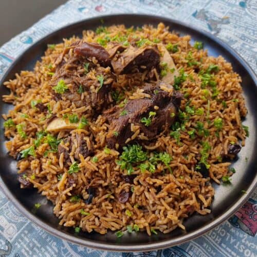 Beef Kabsa with aromatic long-grain rice with different spices garnished with chopped parlsey served in a plate.