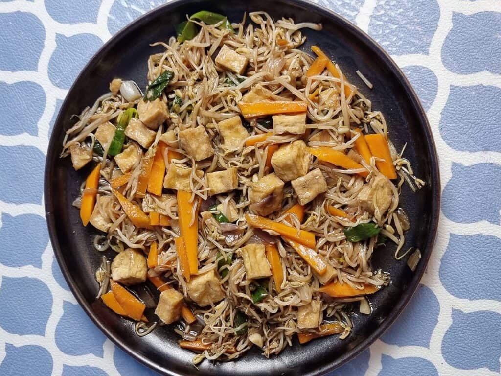 Filipino stir fried vegetable dish Ginisang Togue with Tofu, sliced carrots, bean sprouts, & green onion served on a plate.