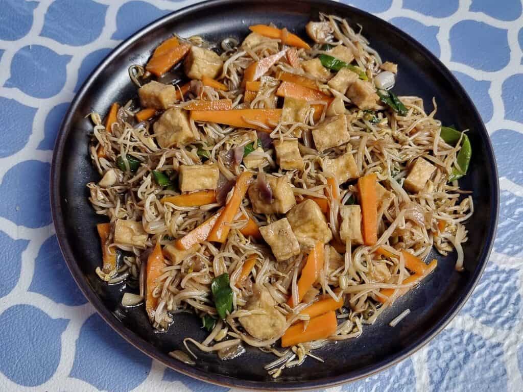 Filipino stir fried vegetable dish Ginisang Togue with Tofu, sliced carrots, bean sprouts, & green onion served on a plate.