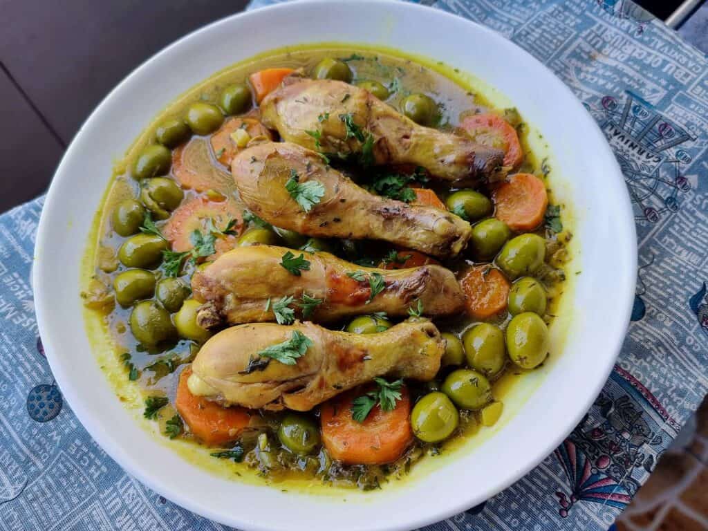 Tajine Zitoune: Algerian chicken stew with carrots, olives, and North African spices served on a plate.