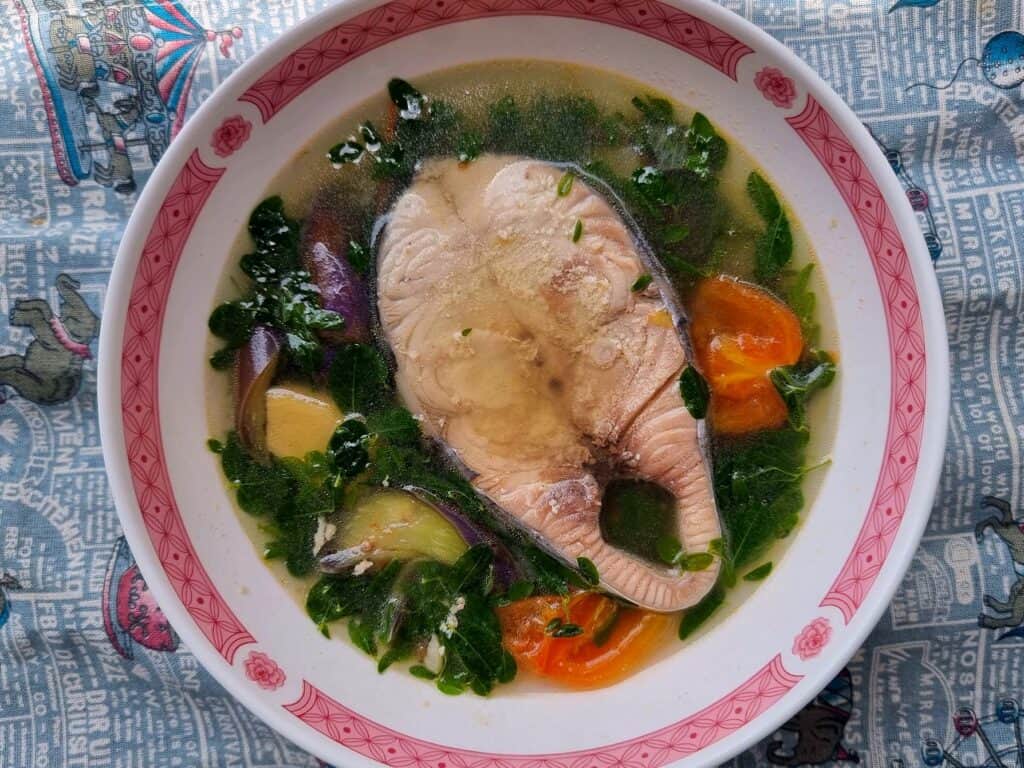 A filipino soup recipe fish tinola containing Spanish mackerel steak, ginger, lemongrass, moringa, and eggplant in a flavorful broth served in a plate bowl.