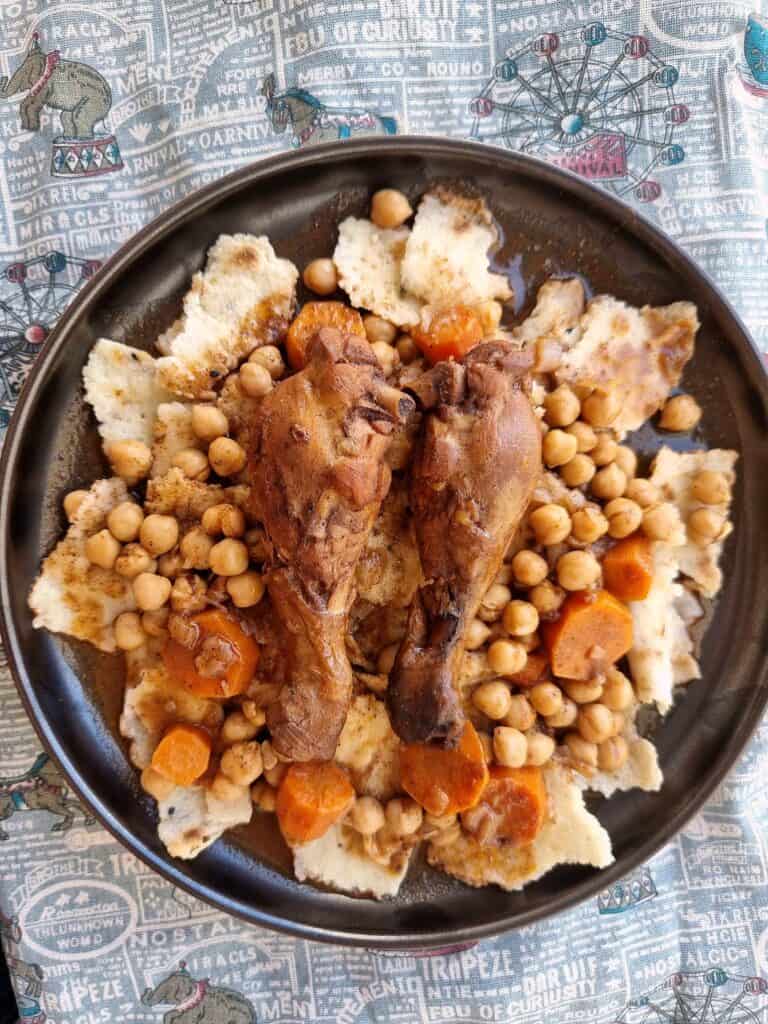 Chakhchoukha, a traditional Algerian dish, presents torn rougag flatbread soaked in a tomato-based broth with chicken, carrots, and chickpeas served on a plate