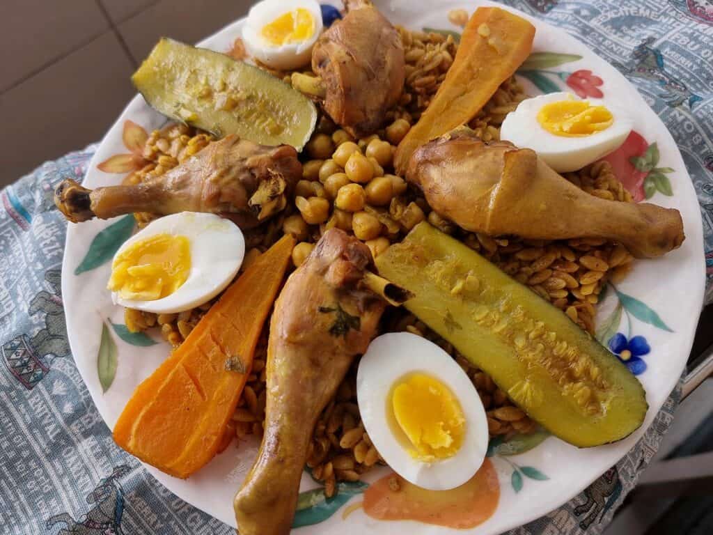An Algerian Tlitli served with chicken drumstick, baton-cut zucchini, carrots, chickpeas in broth, served with layered boiled egg over orzo pasta.