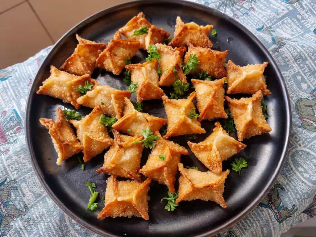 Golden-fried crispy buffalo chicken rangoons with creamy filling garnished with chopped parsley served in a plate.