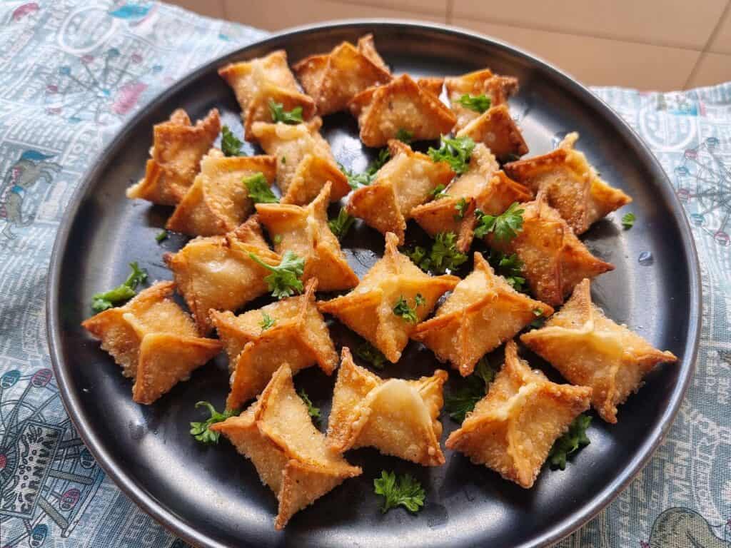 Golden-fried crispy buffalo chicken rangoons with creamy filling garnished with chopped parsley served in a plate.