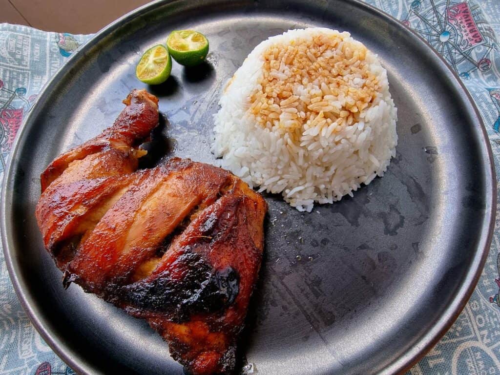 A Filipino bacolod chicken inasal recipe with slices of calamansi and white rice topped with chicken annatto oil served on a plate