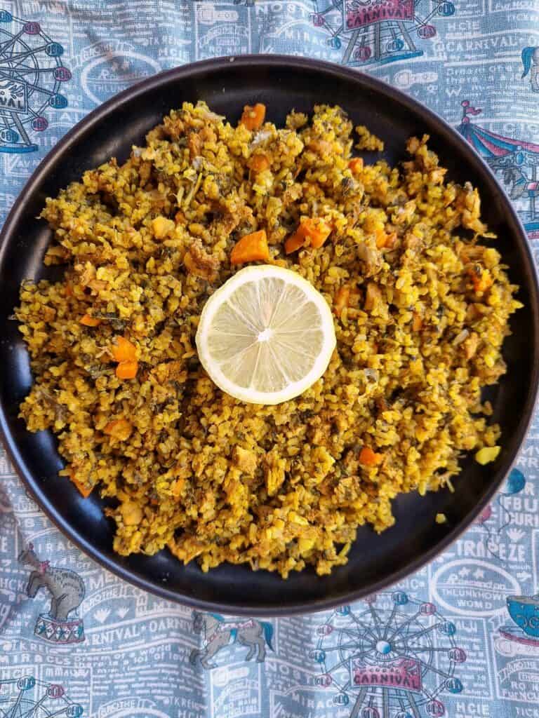 Tunisian recipe Rouz Jerbi (Djerbian rice) mixed with chopped chicken, carrots, chopped green leaves, rice with different aromatic spices with sliced lemon on top of the rice on a plate