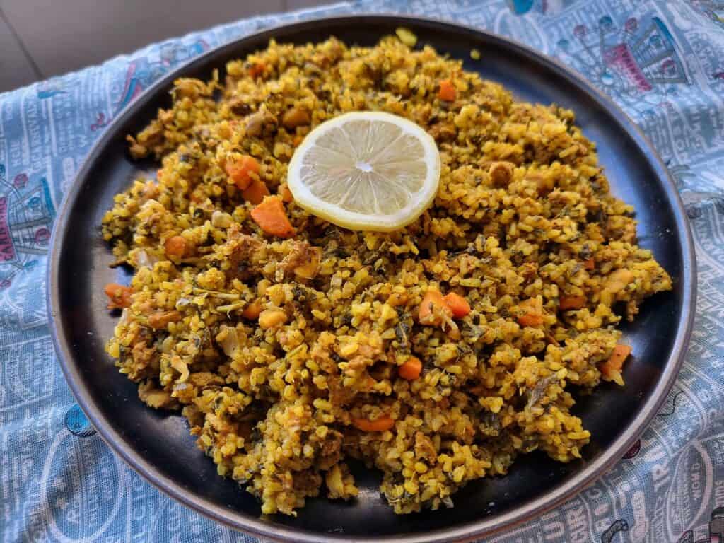 Tunisian recipe Rouz Jerbi (Djerbian rice) mixed with chopped chicken, carrots, chopped green leaves, rice with different aromatic spices with sliced lemon on top of the rice on a plate