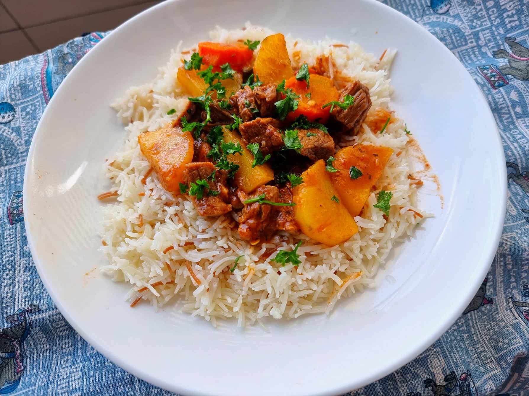 Turkish beef stew tas kebab recipe containing beef fillet, potatoes, carrots topped above rice served on a plate