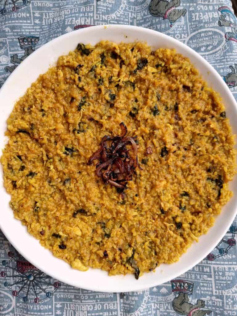 Gulf Arabian rice dish Madrouba with overcooked rice, chicken, tomatoes, herbs, and spices with garnished fried onion in the center serve on a plate.