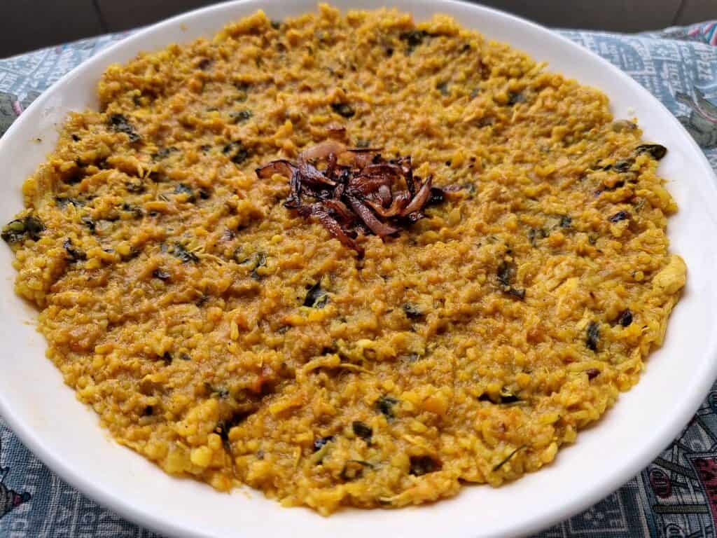 Gulf Arabian rice dish Madrouba with overcooked rice, chicken, tomatoes, herbs, and spices with garnished fried onion in the center serve on a plate.