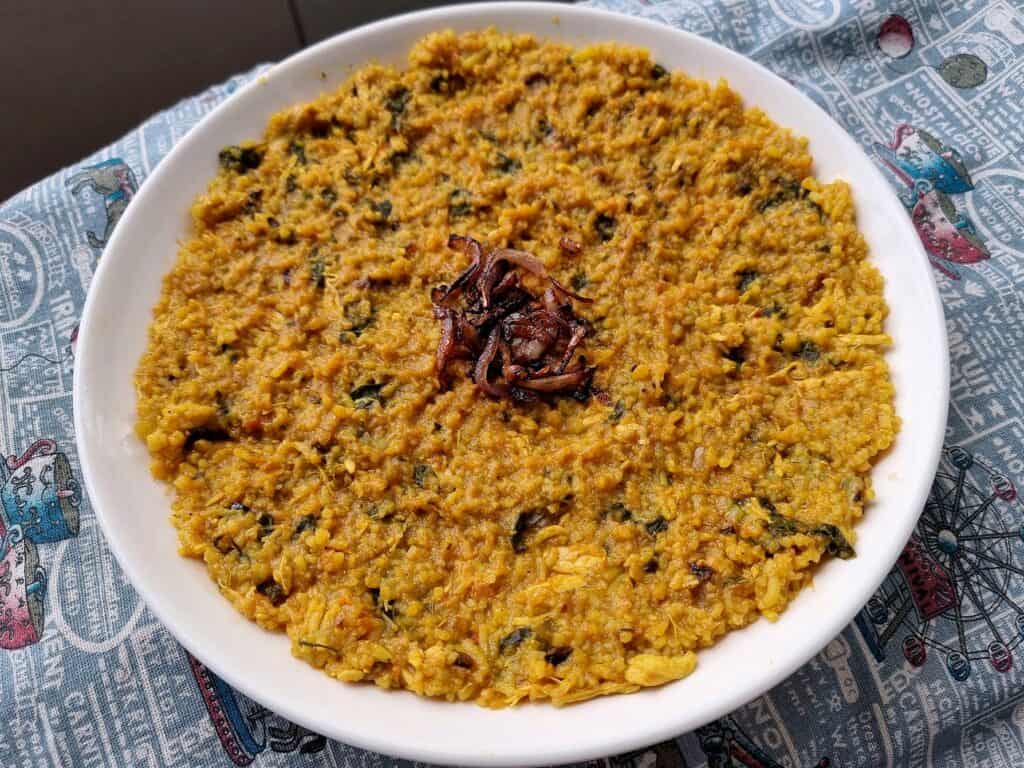 Gulf Arabian rice dish Madrouba with overcooked rice, chicken, tomatoes, herbs, and spices with garnished fried onion in the center serve on a plate.