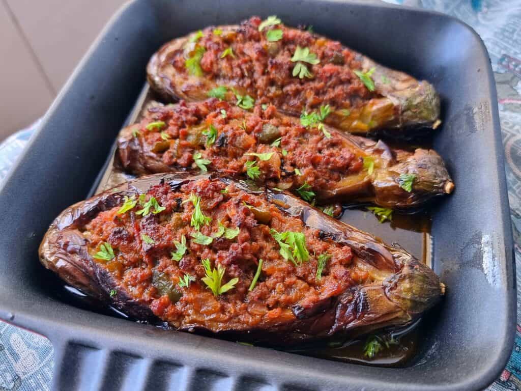 Turkish Stuffed Eggplants called Karniyarik which is stuffed with seasoned ground beef, onions, tomatoes, and green peppers garnished with chopped parsley leaves.