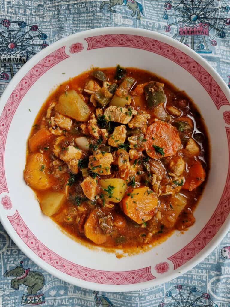 A turkish chicken stew Tavuk Sote that contain chopped boneless chicken breast with carrots and potatoes garnished with chopped parsley cooked in a tomato sauce served in a bowl.